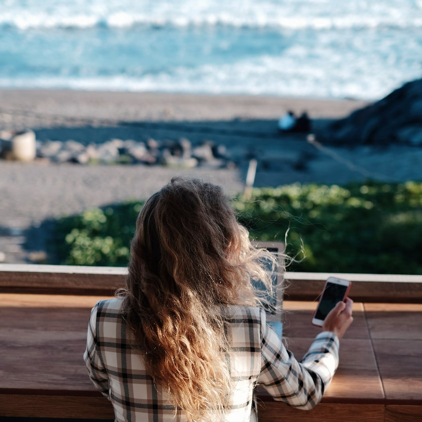 Ragazza di spalle che fa smart working in riva al mare, seguendo le orme della YOLO Economy 